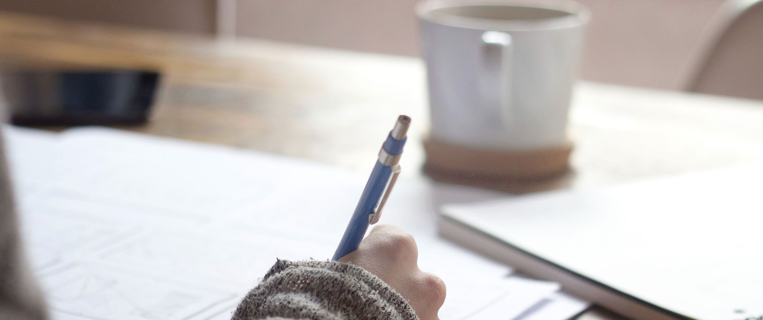 A person's hand holding a pen and writing at a desk